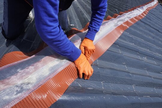 Installation of a roof ridge ventilation and sealing system. A roofer installs a ridge cap on a metal roof. Roofing work. Sandwich panels in the form of tiles.
