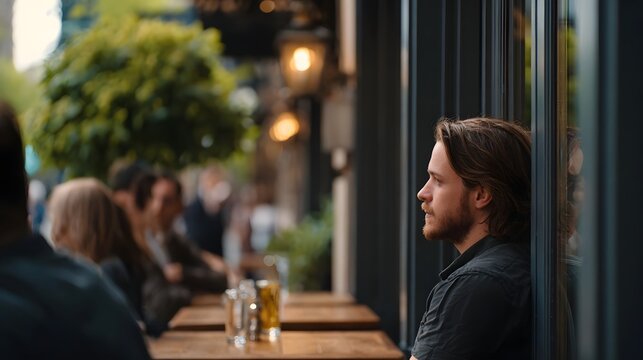 A man sits at an outdoor cafe table gazing thoughtfully into the bustling urban street scene during the day