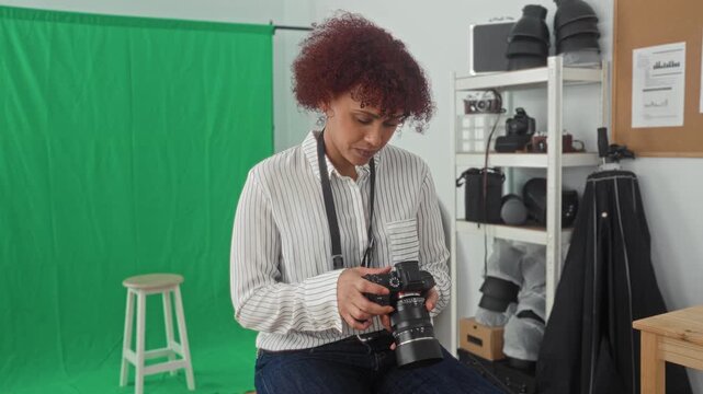 Woman photographer holding camera points finger in studio with green screen and shelving full of equipment; creative confidence.