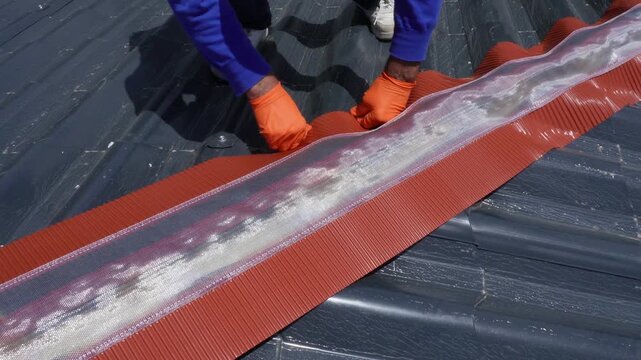 Installation of a roof ridge ventilation and sealing system. A roofer installs a ridge cap on a metal roof. Roofing work. Sandwich panels in the form of tiles.