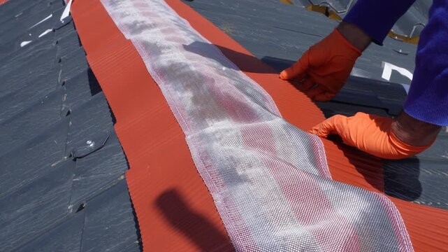 Installation of a roof ridge ventilation and sealing system. A roofer installs a ridge cap on a metal roof. Roofing work. Sandwich panels in the form of tiles.