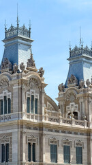 Fototapeta premium Historic Ornate Building In Barcelona With Twin Towers And Sculptural Details, Classical Architecture Facade, Blue Sky Background, Travel And Cultural Heritage Concept