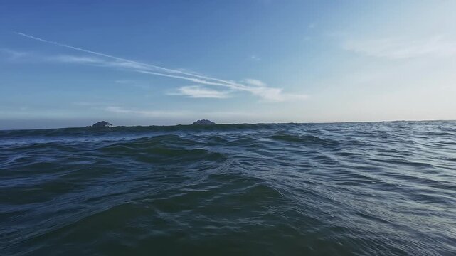 POV of bather tracking ocean waves rolling in from horizon to shore golden droplets spray close as sun sets revealing immersive motion water texture and distant beach backdrop