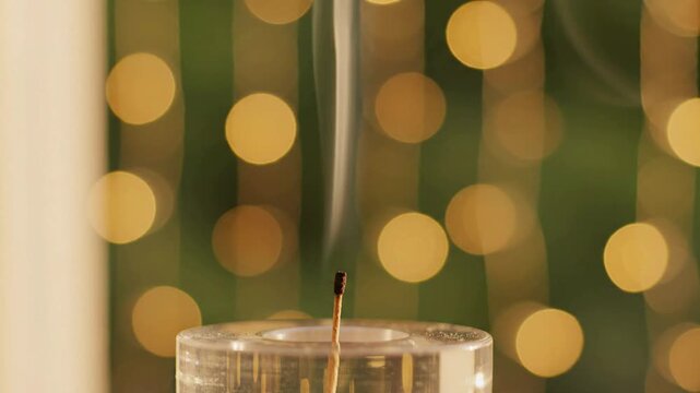 Burning candle wick with wisps of smoke rising against a blurred background of warm golden bokeh lights, evoking atmosphere and serenity