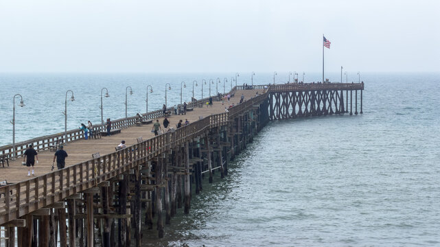 VENTURA BEACH, CA, MAR 30, 2026: High view, looking down at side view of Ventura Pier over water, showing full length with X-brace pilings, visitors, and American flag