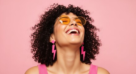 Obraz premium Young woman with curly hair wears yellow sunglasses and pink lightning bolt earrings while laughing.