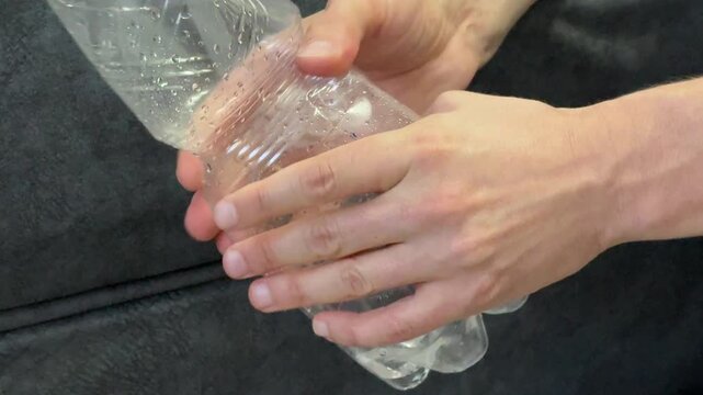 Hands crushing an empty plastic bottle to reduce waste. Environmental pollution, recycling awareness, plastic overuse and sustainability concept in home setting