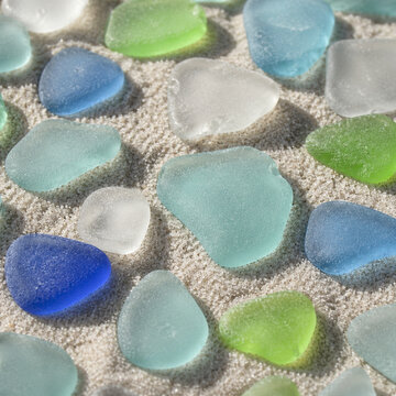 Morceaux de verre de mer color&eacute;s sur sable clair en macro