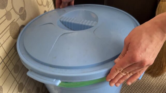 A person opens and closes a round blue plastic trash bin with a snap lid