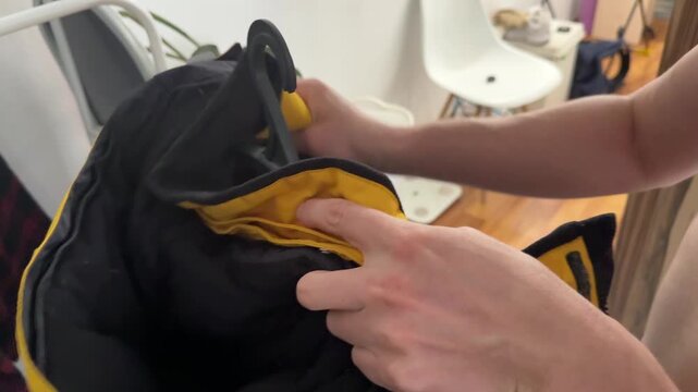 A person hangs a yellow jacket on a black hanger inside a home environment
