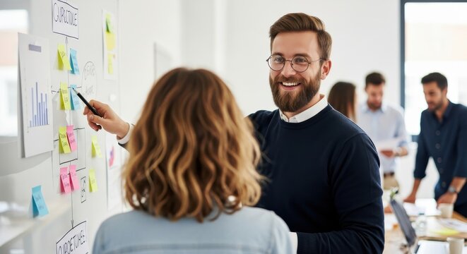 Professional colleagues collaborate on a project strategy using sticky notes on a whiteboard in a modern office.
