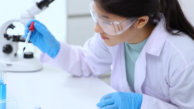 Teen scientist girl conducting science test by carefully evaluating blue solution in laboratory. Science, laboratory, experiment, and research demonstrate academic progress and practical skills.