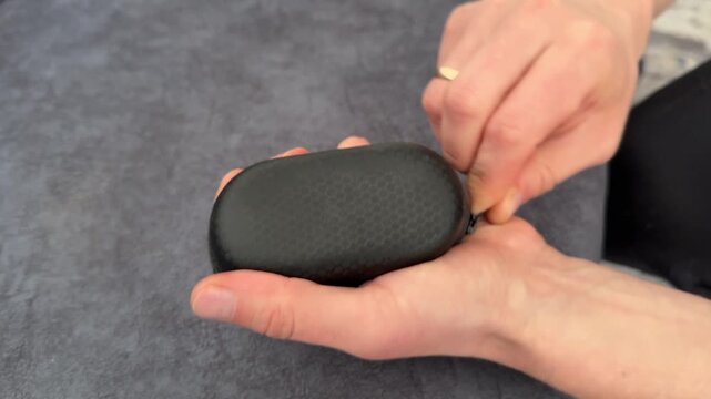 A person carefully unzips a compact black case