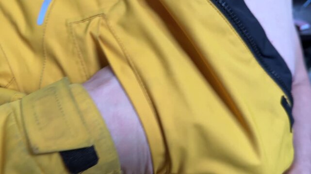 A person inserts and removes their hand from the side pocket of a yellow jacket
