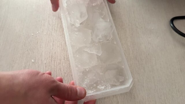 Hands opening plastic ice tray with frozen cubes