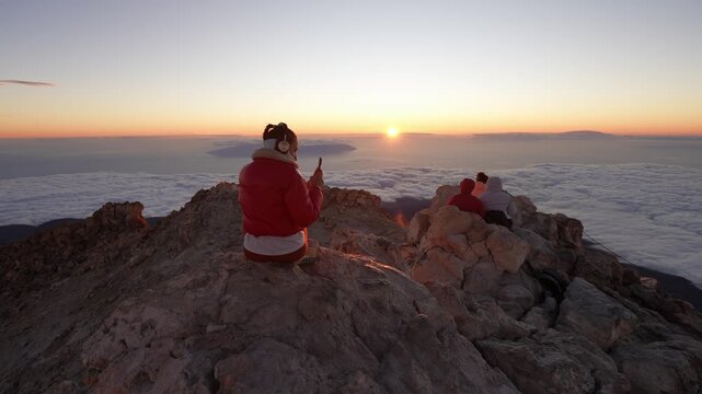 Woman on mountain peak recording a spectacular sunrise with smartphone