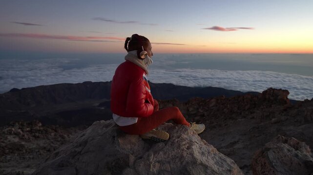Woman watching sunrise above clouds from mountain peak