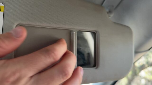 Hand opening and closing the mirror cover on a car sun visor. Close up of sliding panel to reveal vanity mirror inside vehicle interior during everyday driving routine