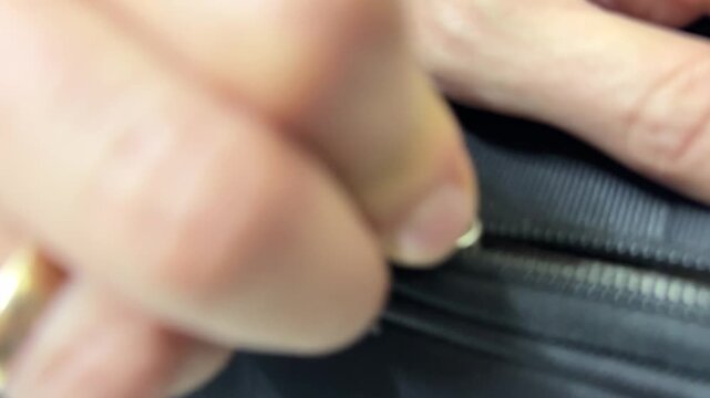 Hand pulling zipper on black suitcase, closing luggage for travel