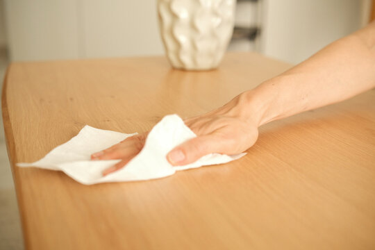 Woman hands wiping dust, cleaning wooden table with disposable cleaning wipes. Everyday household cleaning and hygiene routine at home