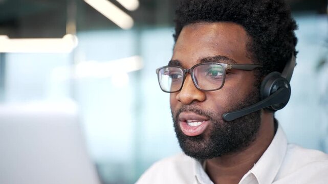 Close up. African american corporate operator in headset working in customer support service on helpline telesale talking using laptop in business office. Agent of call center advises client online