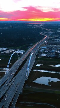 Multiple cars with headlights on move by the Dallas Margaret Mcdermott Bridge at twilight time. Spectacular view of the metropolis from top with colorful sky at backdrop. Vertical video