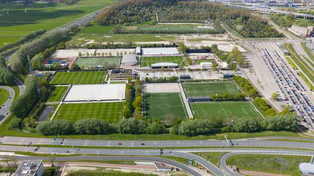 Duivendrecht, Netherlands - 19 April 2026: Aerial view of De Toekomst training ground with multiple football pitches, modern sports facilities, and a large parking area under a clear sky.