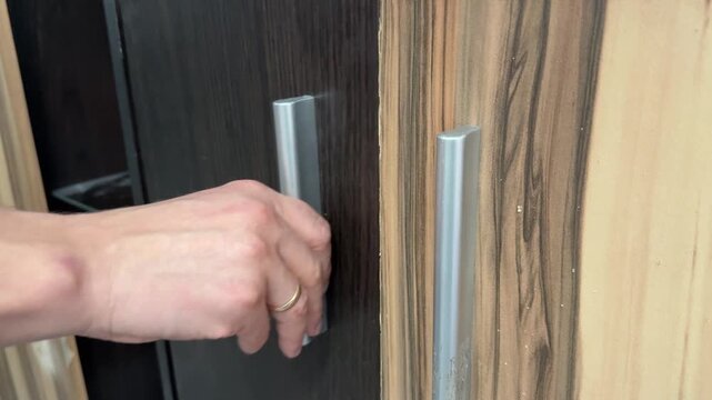 Hand opening and closing wooden cabinet door with metal handle. Home furniture detail and storage access concept, close up interior shot