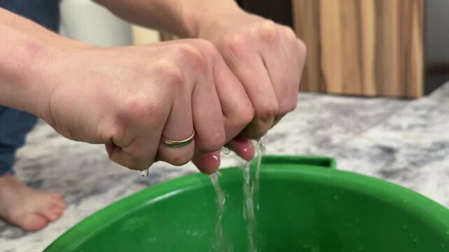 Hands wringing wet cleaning cloth over plastic basin with water. Household cleaning routine, squeezing rag after washing, domestic chores concept