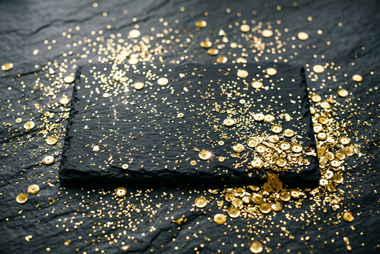 Close up view of golden glitter flakes and sequins scattered on dark textured slate background for artistic festive art
