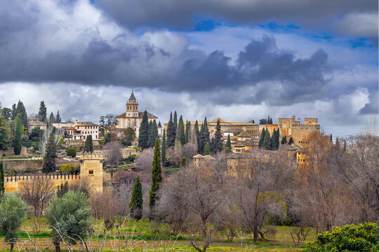 Ancient towers of Alhambra seen from lush Generalife gardens in Granada, Spain. Soft natural light under cloudy overcast sky