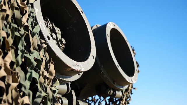 Close Up View of Dual Missile Launching Tubes Elevated at Steep Angle, Military Rocket Launcher System with Camouflage Netting Under Clear Blue Sky