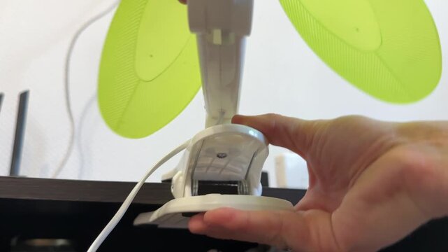 Hand installing small portable fan on desk surface