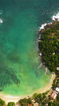 Beautiful sandy beach with palm trees and sea surf with waves. Hiriketiya, Sri Lanka.