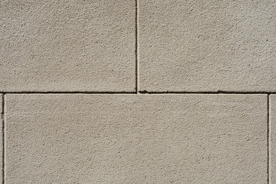 A top down close up view shows the rough and sandy texture of grey rectangular concrete paving blocks with thin dark joints