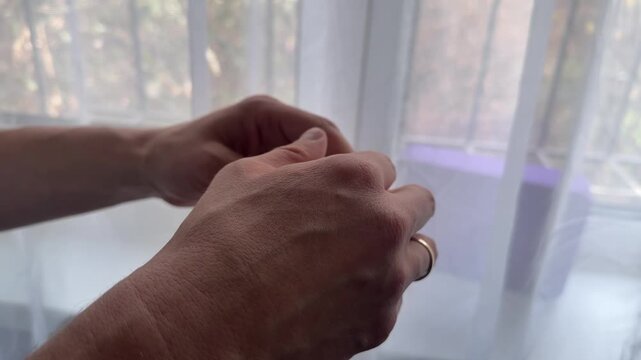 Hands adjust the back strap of a cap, pulling and tightening to fit the head size