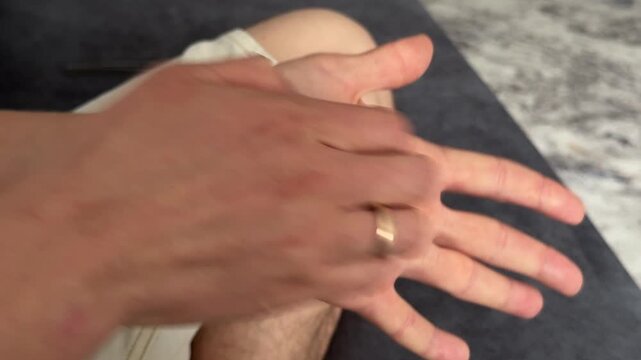 Man vigorously scratches his palm with visible pressure. The gesture suggests itching, irritation, or stress relief. Close-up of hands in natural light, with ring detail on finger