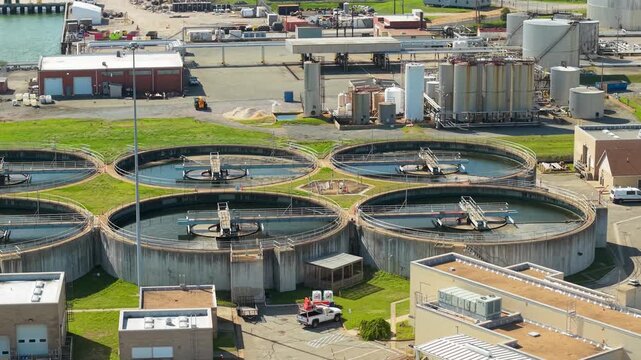 Modern wastewater treatment plant, aerial high-angle orbiting video of large circular primary clarifier tanks, showcasing water purification and industrial utility infrastructure.