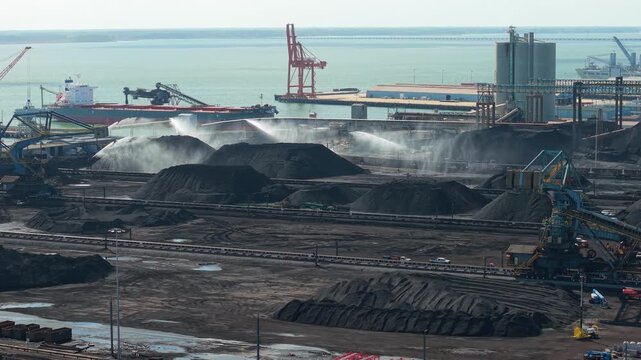 Newport News, Virginia, An aerial perspective of the Dunbar Coal Terminal, featuring industrial water cannons suppressing dust over massive coal stockpiles near the James River waterfront.