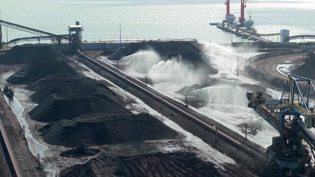 Newport News, Virginia, An aerial perspective of the Dunbar Coal Terminal, featuring industrial water cannons suppressing dust over massive coal stockpiles near the James River waterfront.