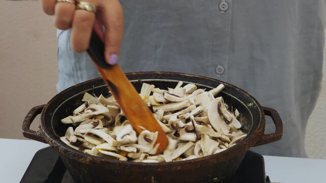 In a deep cast-iron skillet, chicken is fried in vegetable oil with teriyaki sauce and sliced ​​champignons. Medium shot.