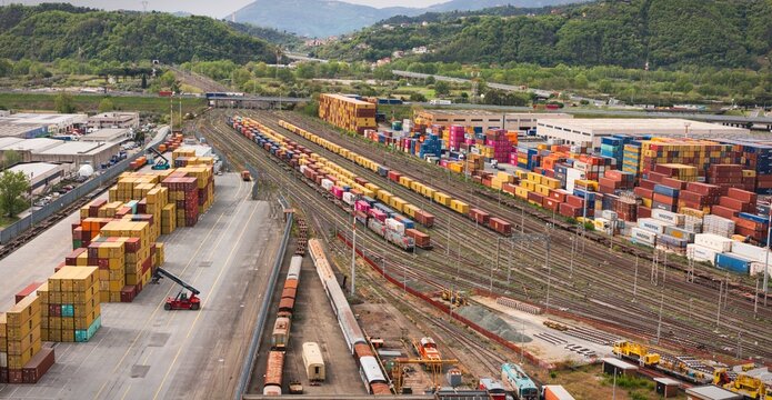 Santo Stefano di Magra, Italy - 18 April 2026: Aerial view of the Retroporto merci freight terminal with colorful shipping containers on trains and tracks against green hills.