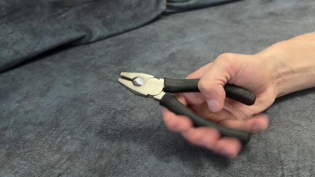 Close-up of hand holding black metal pliers over gray surface. DIY or repair tool in casual home setting. Focus on grip and texture, concept of manual work or utility