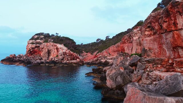 Reddish rocky cliffs and turquoise waters create a stunning landscape at cala des moro in mallorca, spain