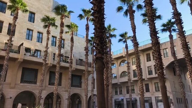 A historic courtyard in Old Jaffa surrounded by ancient stone buildings, with tall palm trees growing in the center during the daytime.