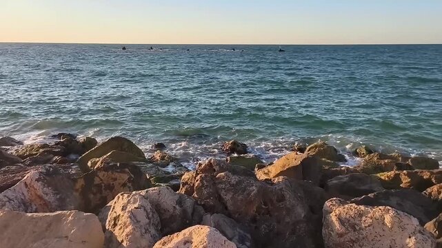 Dynamic daytime footage of a deep blue, turbulent sea with waves in constant motion. rugged shoreline covered with numerous stones in front