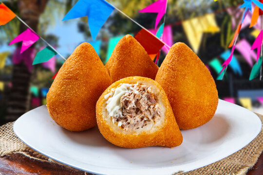 Delicious Brazilian chicken coxinha with creamy catupiry cheese, served on a white plate. Traditional savory snack for Festa Junina celebrations with colorful party flags in the background.