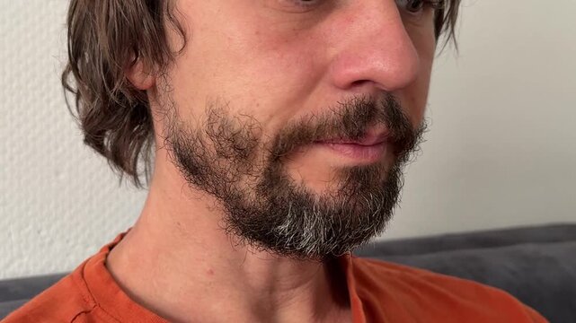 Man hiccups and swallows saliva with eyes closed. Subtle tension in throat and lips. Beard and mustache visible. Natural indoor expression tied to reflex or discomfort