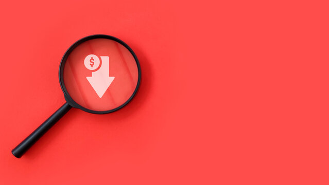 Magnifying glass focusing on downward arrow with dollar icon on red background, representing financial loss, decline, and risk analysis.