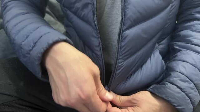 Close-up of hands zipping up a dark blue puffer jacket. Everyday clothing gesture for warmth, comfort and casual winter preparation at home